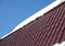 Country house roof from brown metal tile with snow in sunny spring day under blue sky