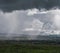 Country landscape before the storm, with rain clouds and precipitation over the town, the sky has a sun ray.