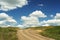 Country road ending in blue sky with big cumulus clouds