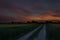 Country road among green fields, colorful clouds at sunset