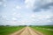 Country unpaved road among green fields and blue sky