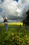 Country womanat farm gate watches the clouds over golden crops and fields