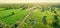 Countryside road with wheel traces in rural areal with green fields and distant hills at sunset. Aerial countryside landscape