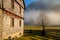 Countryside rural nature scene with wooden house architecture in foggy landscape