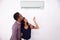 Couple Adjusting Temperature Of Air Conditioner