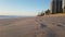 A couple of adults walking on a sandy beach. City, buildings, beach in the early morning, at dawn.