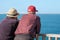 Couple of aged people looking at the ocean on vacations. Wearing a cap, hat and comfortable clothes. Grey nomads looking at the