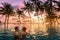 Couple at beach vacation holidays resort relaxing in swimming pool with scenic tropical landscape at sunset, romantic summer