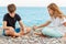 Couple of beautiful teens, first love. Girlfriend and boyfriend sitting on the beach and playing with pebble stones