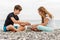 Couple of beautiful teens, first love. Girlfriend and boyfriend sitting on the beach and playing with pebble stones