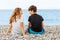 Couple of beautiful teens, first love. Guy hugs a girl sitting on the pebble beach next to each other and looking at the sea.