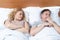 Couple in bed, disgruntled woman looks at a man who turned the other way. Relationship concept.