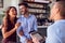 Couple Being Greeted By Maitre D Using Digital Tablet As They Arrive At Restaurant