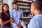 Couple Being Greeted By Maitre D Using Digital Tablet As They Arrive At Restaurant