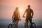 Couple bicyclist with mountain bikes on the hill at sunset