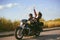 Couple of bikers ride across the field. A man drives a motorcycle, a girl listens to music with headphones on the road. The joy of