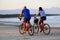 A couple biking on the beach sand in front of the sea. Itaguare beach, Bertioga, Brazil