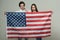 Couple on calm faces holds flag of USA. Couple welcomes to visit USA. Guy and girl proud to be americans, grey