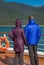 Couple in colorful purple and blue winter puffer jackets view Alaska, USA coastl from ship`s deck on a sunny cold day.