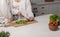 Couple cooking at home. Woman cutting vegetables for salad in modern white scandi kitchen. Healthy food concept.