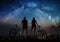 Couple cyclists with mountain bikes at night under starry sky