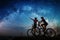 Couple cyclists with mountain bikes at night under starry sky