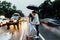 The couple embraced under an umbrella rain, stands on the road. Cars are passing by.