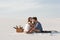 Couple embracing while sitting on blanket with basket of fruits and acoustic guitar on beach