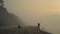 Couple enjoying sunrise on beach. Man sitting on shore. Woman walking along sea