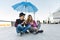 Couple friends sitting under an umbrella and looking at smartphone
