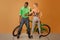 couple in front of a bycicle on orange background