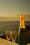 A couple of glasses of champagne next to a bottle of sparkling wine with the sea in the background