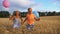 Couple of happy little kids with balloons in arms jogging through wheat field. Small girl and boy holding hands of each