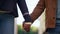 Couple holding hands together walking at defocused street sky background closeup