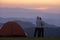 Couple is hugging each other by the tent during overnight camping while looking at the beautiful scenic sunset over the mountain