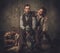 Couple of hunter with a english setter and shotgun in a traditional shooting clothing, sitting on a dark background.