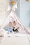 Couple infant boys of 1-year old playing in toy tent with garland at nursery.