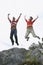 Couple Jumping With Arms Raised Over Rock