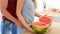 Couple in a kitchen slicing red watermelon. Couple in their large contemporary white kitchen