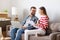 Couple with laptop and papers sitting on sofa in room with packed boxes and discussing insurance contract after relocation into ne