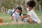 Couple little girls African and Caucasian kids wear face mask while sitting and playing wooden blocks toy in green park together