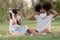 Couple little girls African and Caucasian kids wearing face mask while sitting and playing wooden blocks in green park together