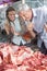 Couple Looking At Meat Through Cabinet In Butchery