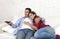 Couple in love cuddling on home couch relaxing watching movie on television with man holding remote control