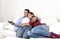 Couple in love cuddling on home couch relaxing watching movie on television with man holding remote control