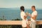 Couple in love drinking juice on balcony, nature and sea on background. Man and lady in bathrobe hold glass with drink