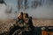 Couple in love sits at outing in NBC protective suits near removed gas masks on smoke background