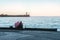 A couple in love sitting on the beach, looking at the old lighthouse in the distance. View of the coastline in the evening at