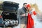 Couple in love sitting in car trunk drinking hot tea in snowy winter forest and chatting. People relaxing outdoors during road
