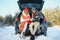 Couple in love sitting in car trunk drinking hot tea in snowy winter forest and chatting. People relaxing outdoors during road